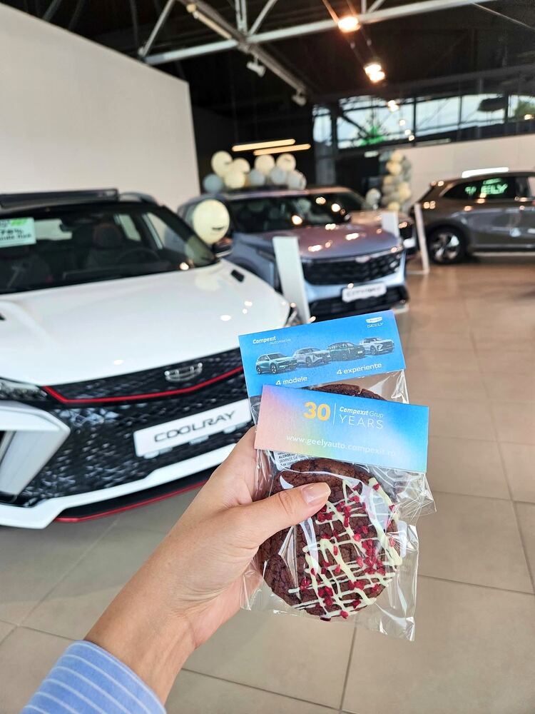 Mână care ține un stroopwafel ambalat, într-un showroom auto