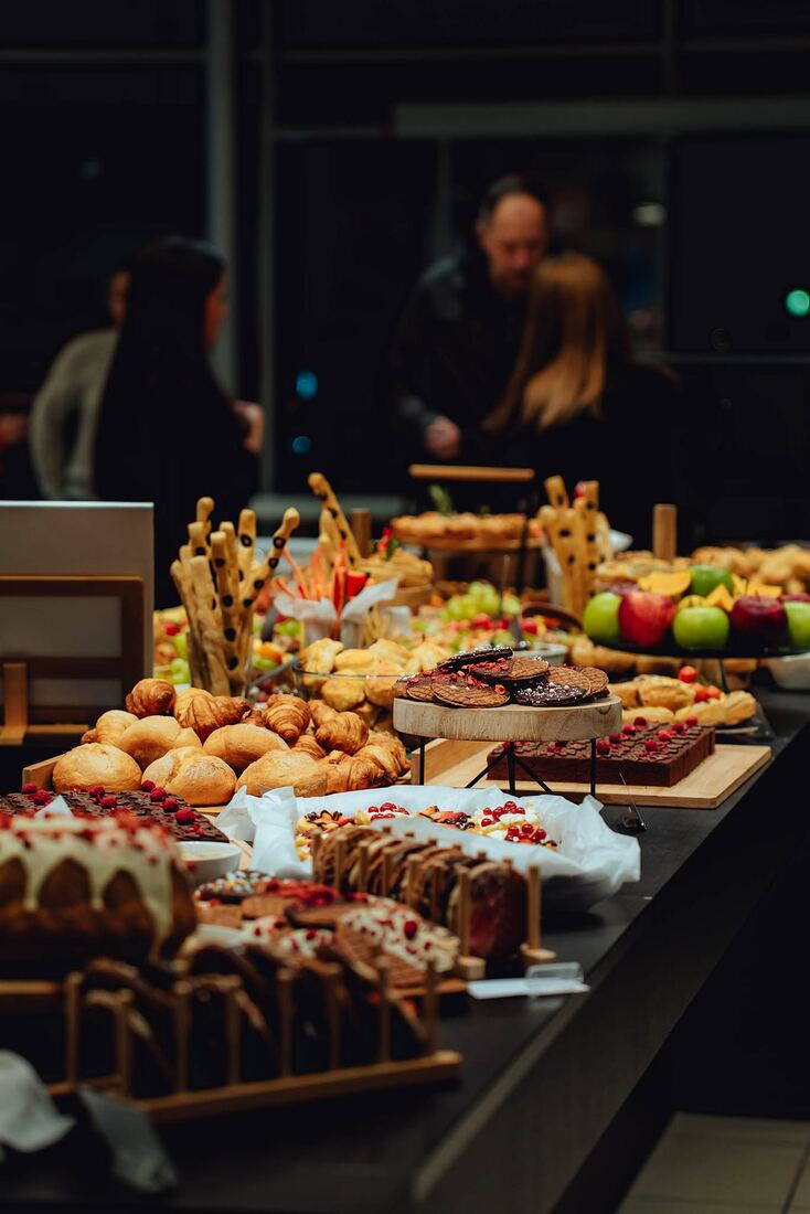 Masă festivă lungă, într-un spațiu de eveniment, cu invitați în fundal