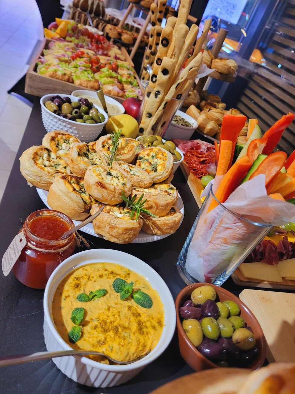 Masă de eveniment cu mini quiche, legume proaspete, sosuri și grisine