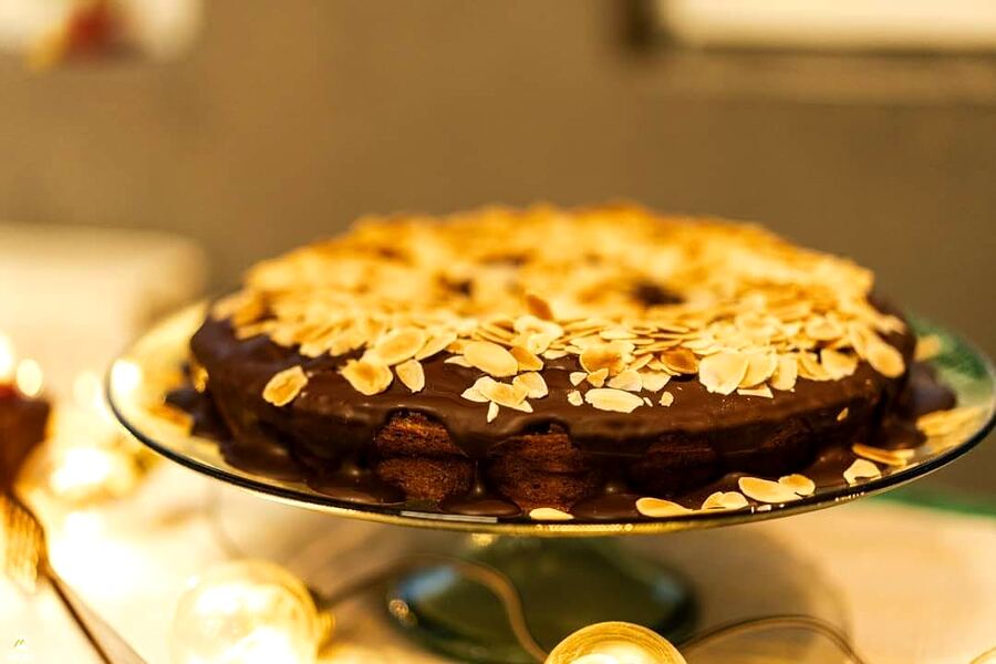 Tort rotund cu glazură de ciocolată și fulgi de migdale, pe un platou înalt