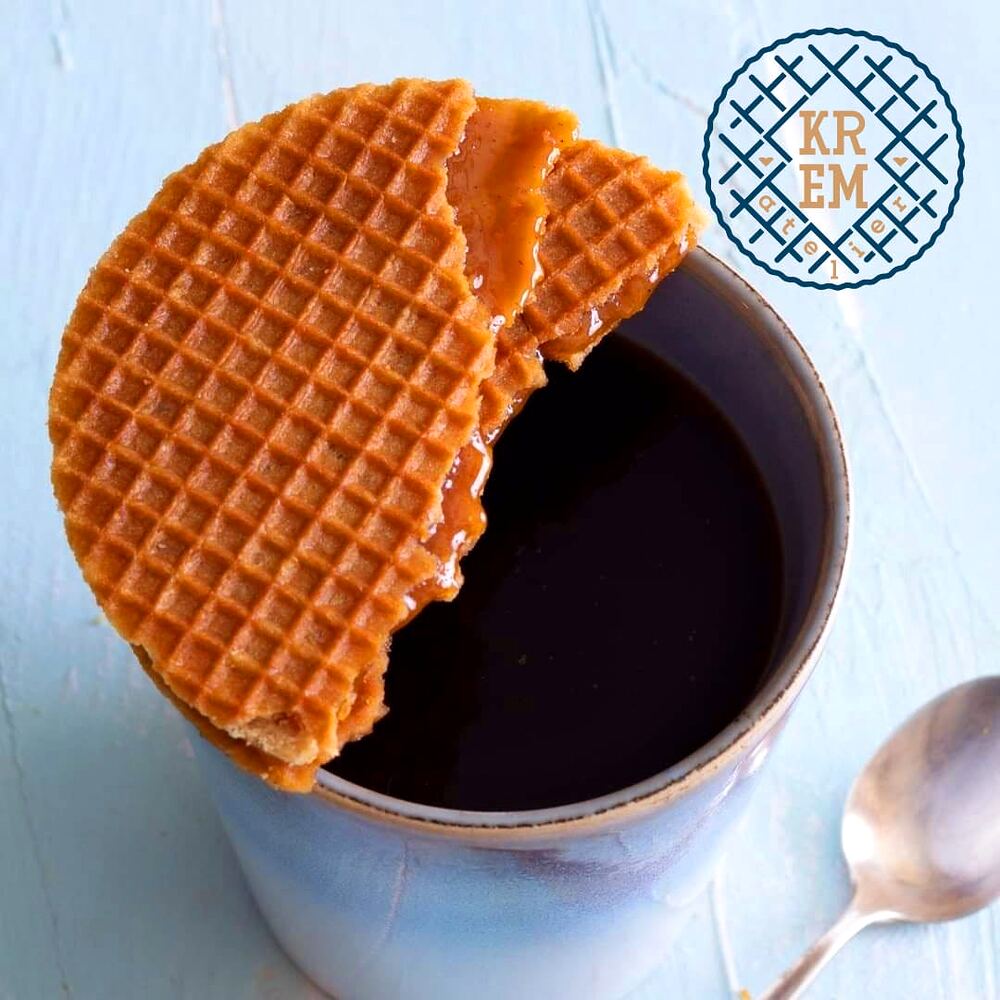Stroopwafel rupt în două, ținut deasupra unei căni de cafea